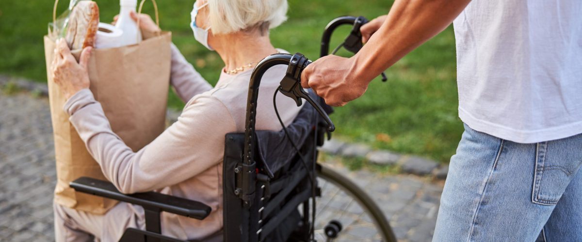 Betreuung von Senioren, Pflegeversicherung, Mann schiebt Seniorin im Rollstuhl